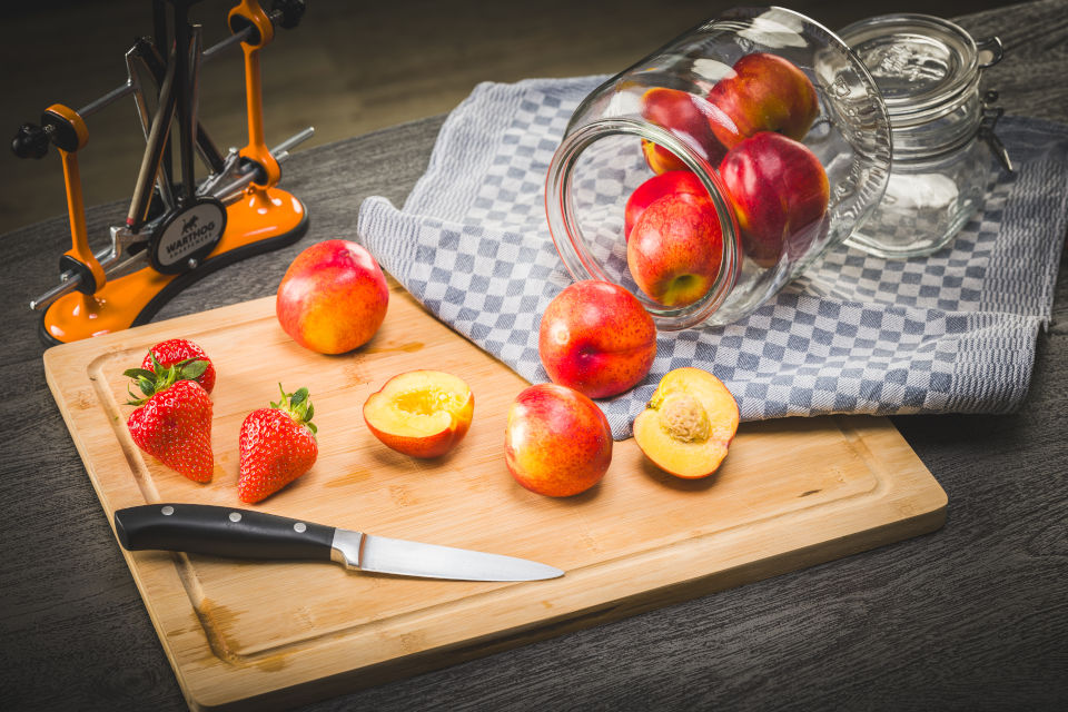Pfirsiche, eine davon mit dem Messer geschnitten und Erdbeeren auf einem Brett, V-Sharp A4 Orange im Hintergrund
